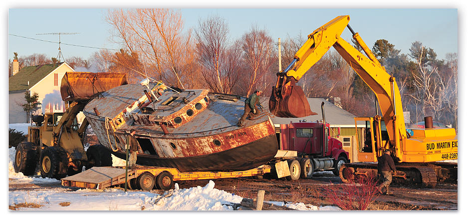 An excavator and terex loader lift the Ruby Ann from her icy dock onto a flatbead trailer for transport to Whiskey Point where the ice is thinner